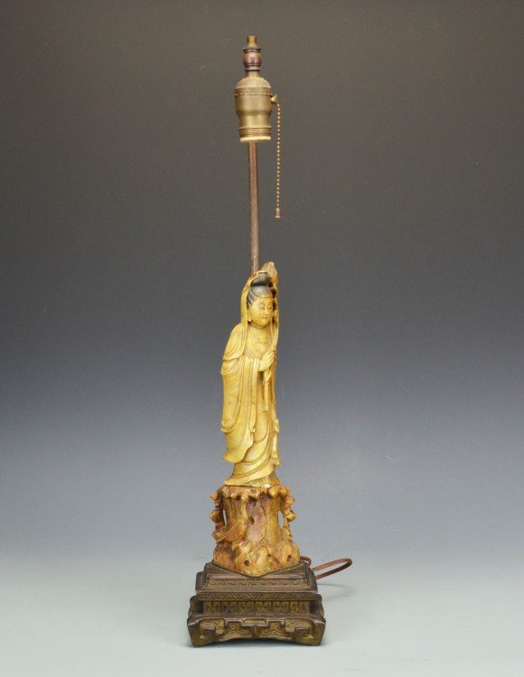 A Soapstone Figure of White Robed Guanyin as Lamp: Standing on a carved rock, the white-robed Guanyin Bodhisattva wearing jewelry and holding a lotus flower, is mounted as a lamp with metal fixtures. With a crack to the base Guanyin is standing on, an