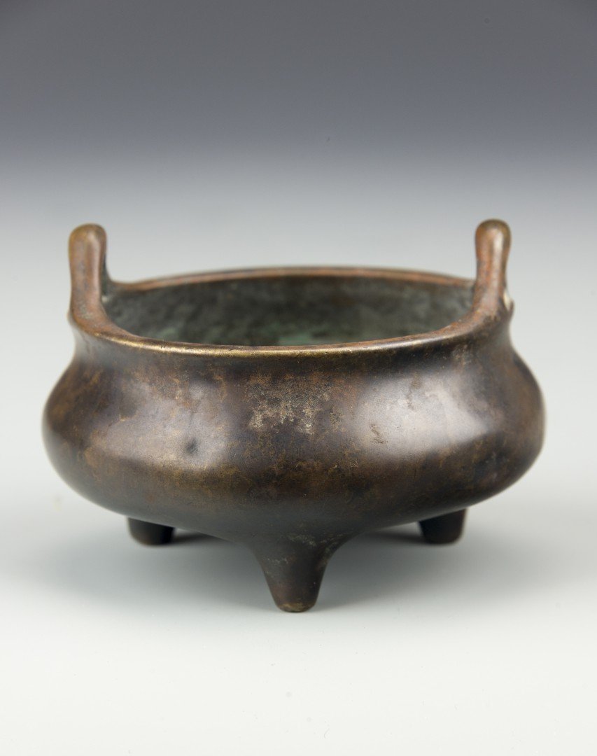 A Chinese Small Bronze Ding Tripod Censer: 19th century, Qing dynasty. Ming-style simply cast tripod censer with two raised handles on opposing sides of the rim. Dark patina. With six-character "Da Ming Xuande nian zhe" mark to base. One old s