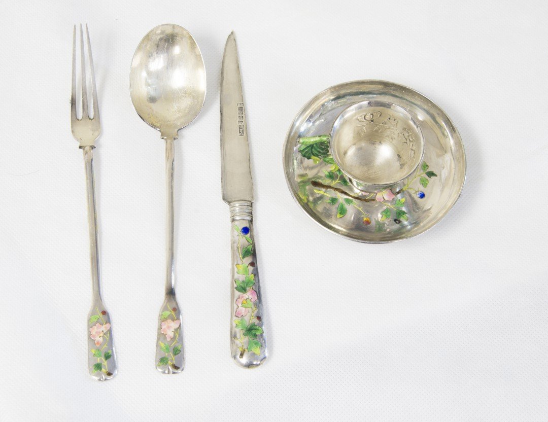 A Chinese Enameled Silver Dinnerware Set: Early 20th century, Qing dynasty. A five-piece silver set consisting of a knife, fork, and spoon, along with a leaf-handled teacup and saucer. All decorated with polychrome enamels to depict leafy flo