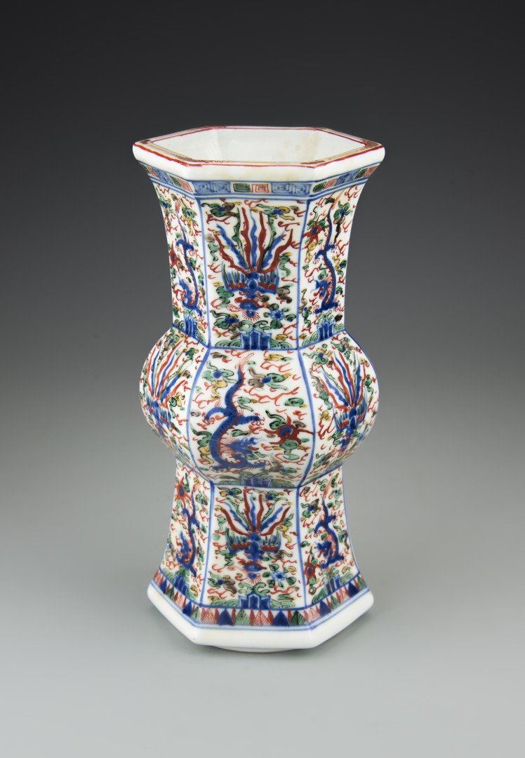A Japanese Wucai Porcelain Gu-shaped Vase: 19th century, Edo period. Imitating Chinese wucai, the hexagonal faceted gu shape altar vase with bulbous center and flaring base and neck, each panel decorated with dragons and phoenixes amid scrolli