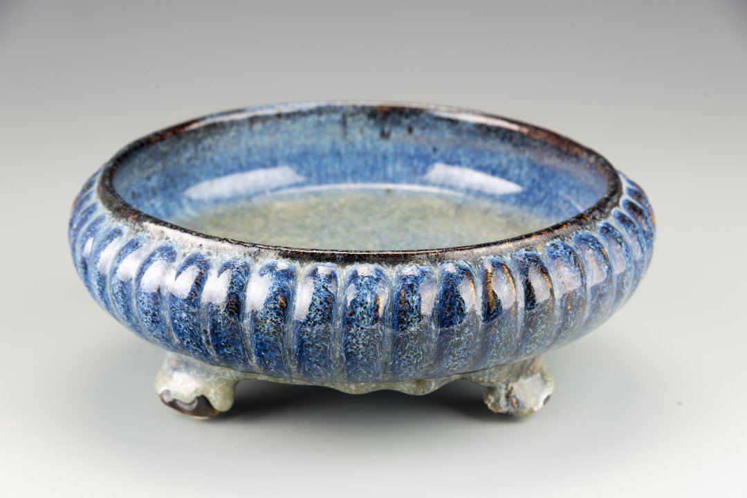 A Chinese Hare's Fur Glazed Bowl: The shallow bowl with a scalloped exterior and thick blue glaze pooling at the three raised feet, with unglazed and unmarked base. Approx. 3 1/4 by 8 7/8 in. diam., 8.4 by 22.6 cm. diam.