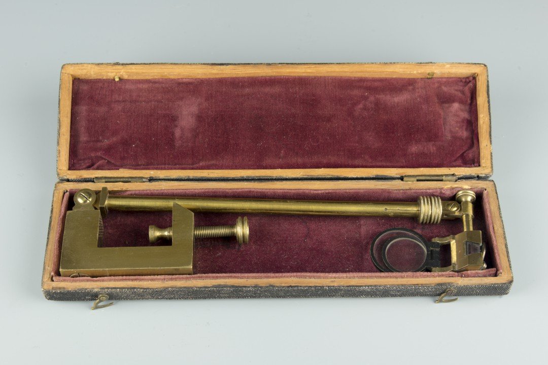 A Small Engineering Tool, 19th century: The brass tool with two small magnifying glasses, with ability to fit the lip of a desk, with original velvet lined box. Approx. 10 1/4 by 2 in., 26.1 by 5.1 cm.