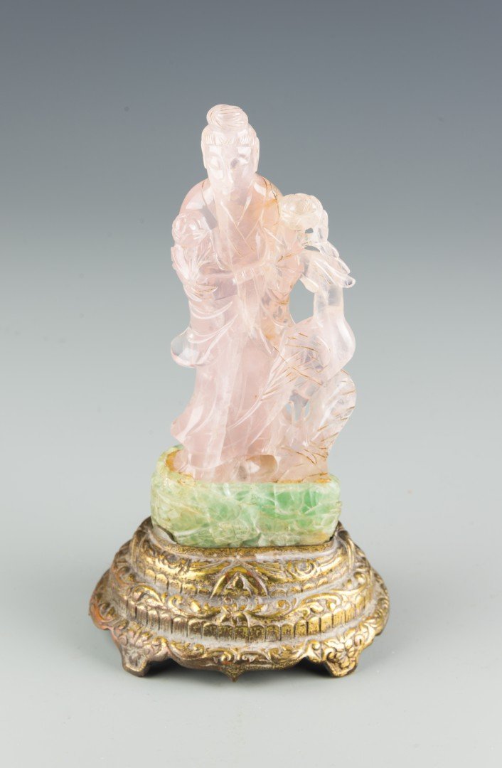 A Rose Quartz and Aventurine Carved Statue: A rose quartz carving of the bodhisattva Guanyin who stands wearing long draping robes and holding a lotus flower, with a phoenix next to the deity with a lotus flower in its mouth, all on a base of g