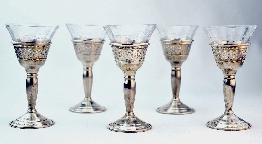 A Set of Five Cartier Sterling Silver and Crystal: Set of five Cartier sterling silver and crystal cordials, the reticulated pedestal base frames fitted with etched floral spray glass liners. Marked Cartier Sterling.