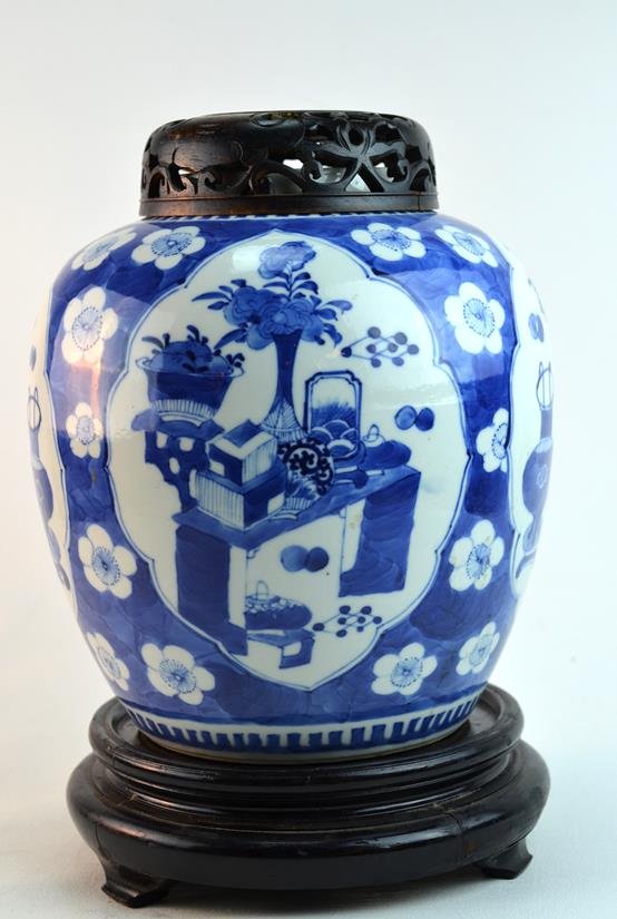 Chinese Blue and White Jar with Wooden Stand: Chinese Qing Dynasty blue and white jar boldly painted with flowers, tables, lanterns, and screens, on a finely carved wooden stand and cover. Four-character mark. 9 1/2" x 9", cover or stand, 2"