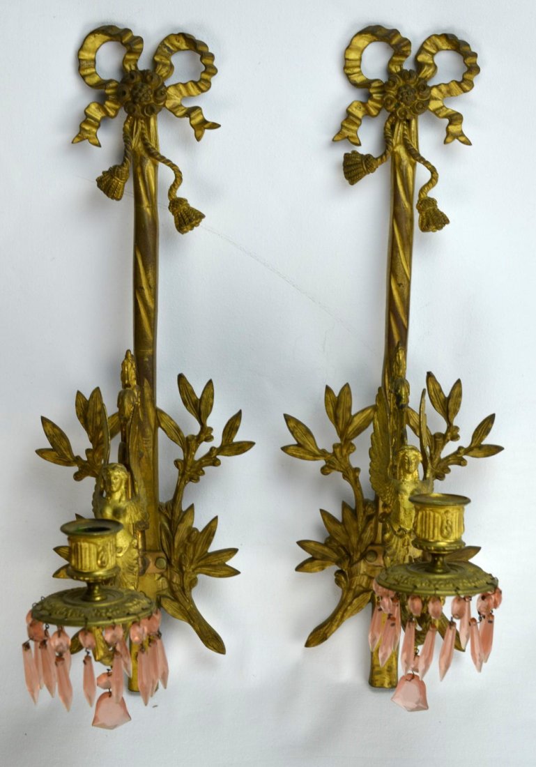 BRASS CANDLE SCONCES Pair of wall-hanging candles: BRASS CANDLE SCONCES Pair of wall-hanging single candleholders with bows, leaves, and angels, the sconce accented with hanging pink cut glass drops. Unmarked. 18'' x 8''