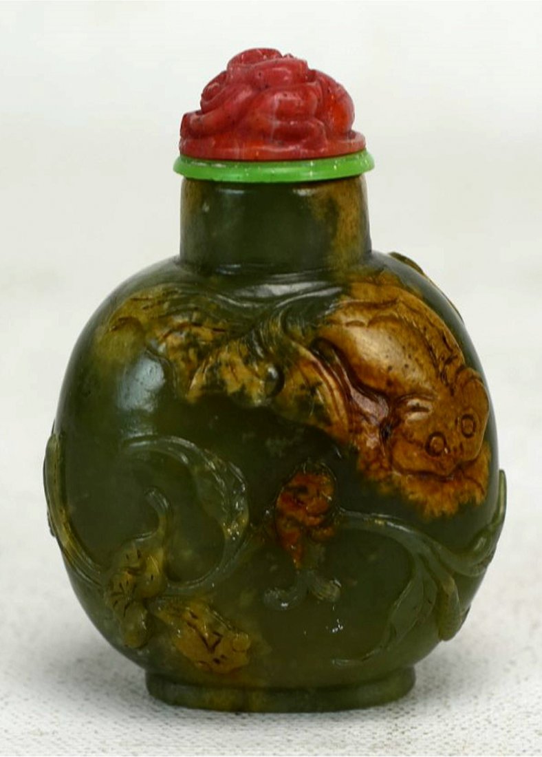 Chinese Carved Green & Russet Jade Snuff Bottle: A Chinese green and russet jade snuff bottle carved with a scrolling design and fish. An in tact coral stopper carved into the shape of a flower. 18/19th century. Height - 2 5/8''