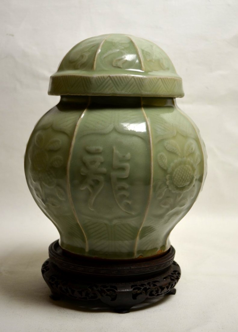 Ming Dynasty Longquan Ginger Jar: A longquan glaze ginger jar in perfect condition. Decorated with Chinese characters, fish, and flowers. A lotus design surrounds the rim and neck. Ming Dynasty. Complete with carved wooden stand. Prov