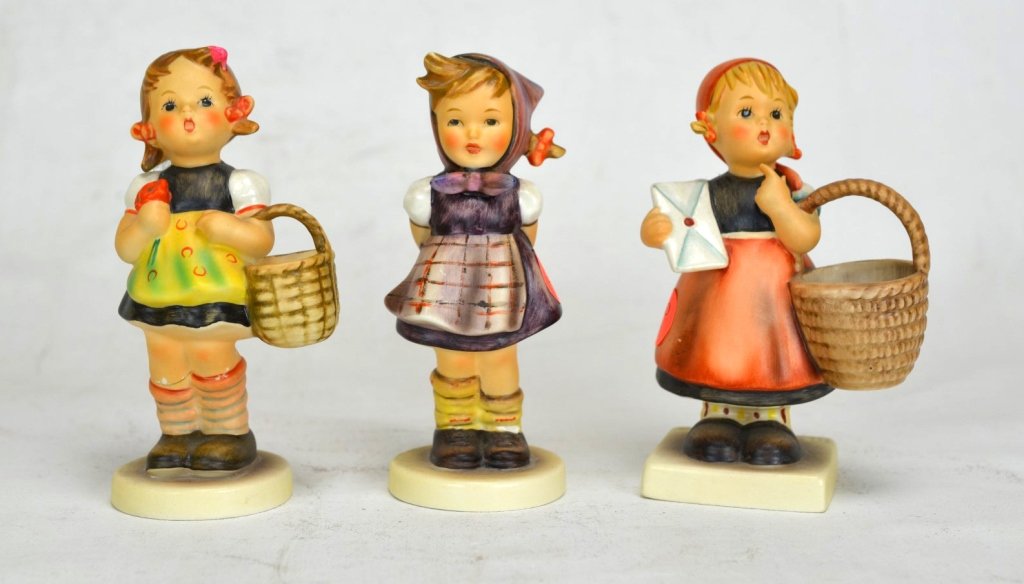 Three M.J. Hummel Goebel Figurines of Girls: Three Goebel figurines by M.J. Hummel. All of girls standing, mouths agape. Two of them holding baskets. Two with repairs to the legs. Height of tallest - 5 1/2"