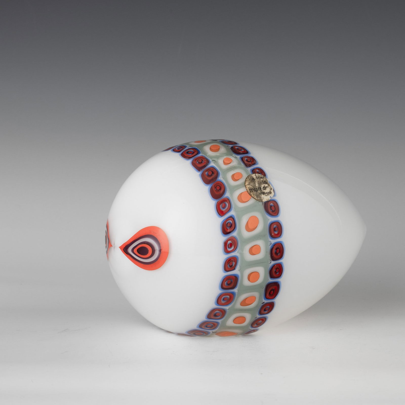 La Murrina, Murano, 1970 ca.: Stylised fish ornament in 'lattimo' (milky) glass decorated with polychrome murrine band.Manufacturer's label. Lunghezza cm 20 altezza cm 14