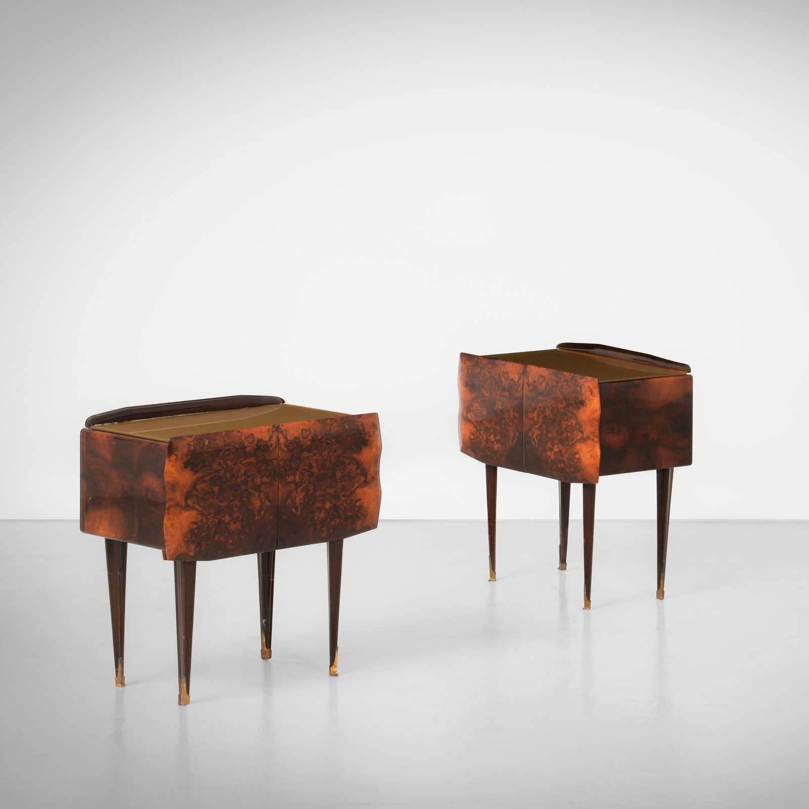 Due comodini: Struttura in legno e impiallacciatura di radica. Piano in vetro colorato e cristallo specchiato. Maniglie, puntali e dettagli in ottone. Prod. Italia, 1950 ca.