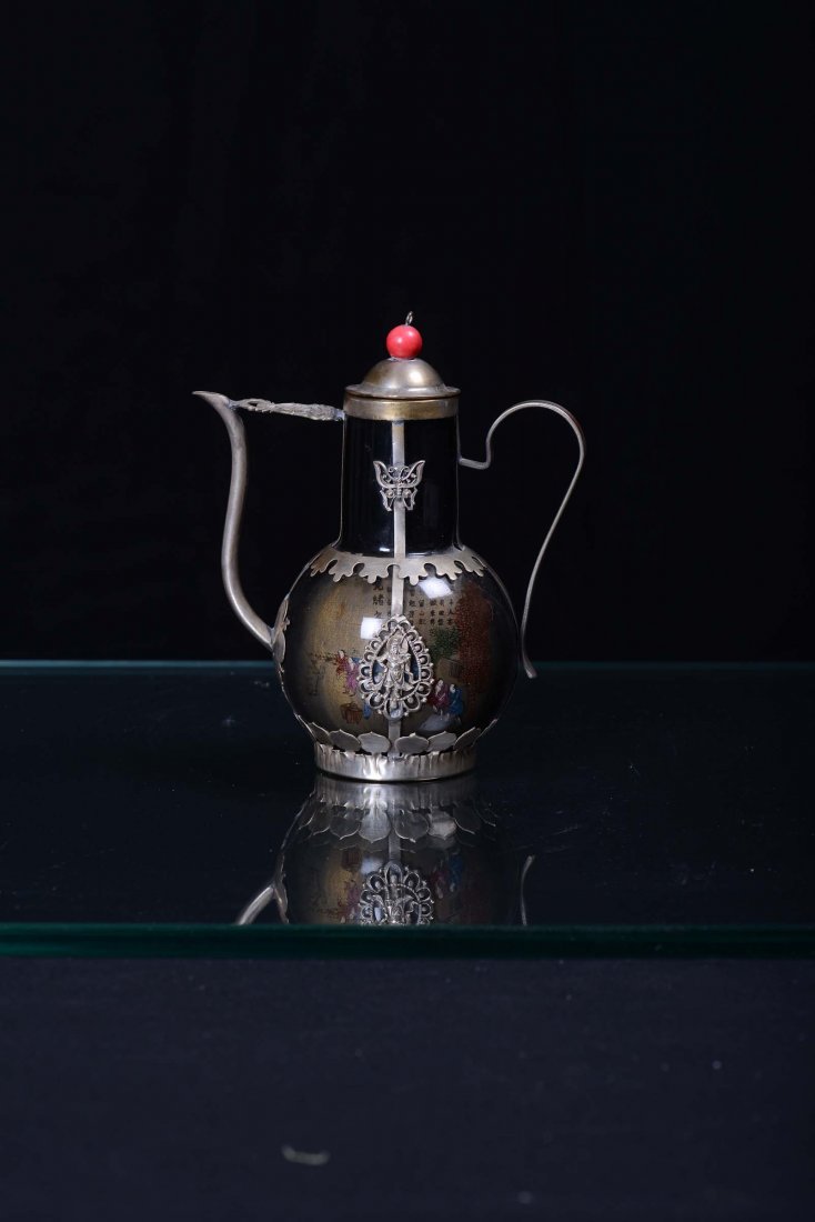 A small glass and metal teapot decorated with figures a