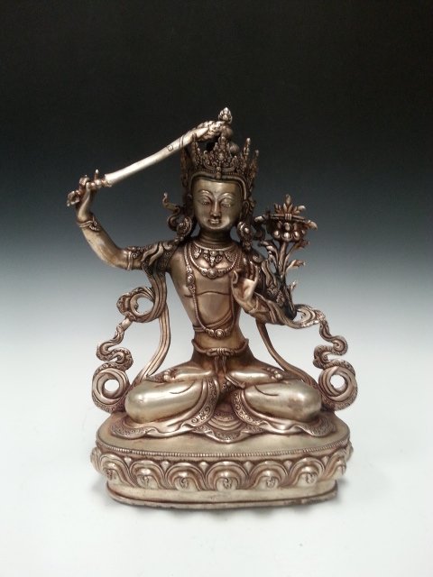 A WEAPON HOLDING SILVER BUDDHA: A buddha holding a weapon with right hand and is pointing is kind of upward. Sitting on a lotus stand. H 7.5" (HJ)