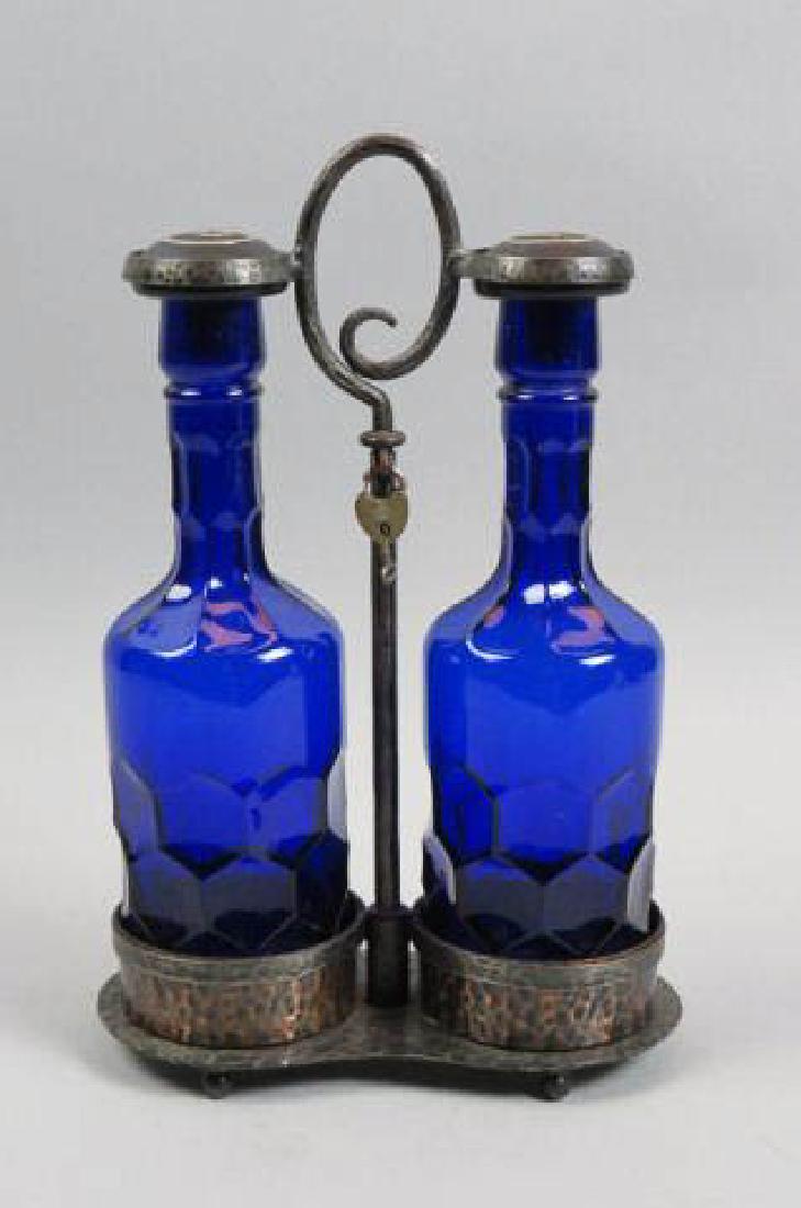 Arts & Crafts Era Tantalus with Cobalt Decanters,: in hand hammered copper finish locking holder, "Scotch" & "Rye," label of Roos Brothers, California, 11" decanters, center handle, 13" tall.
