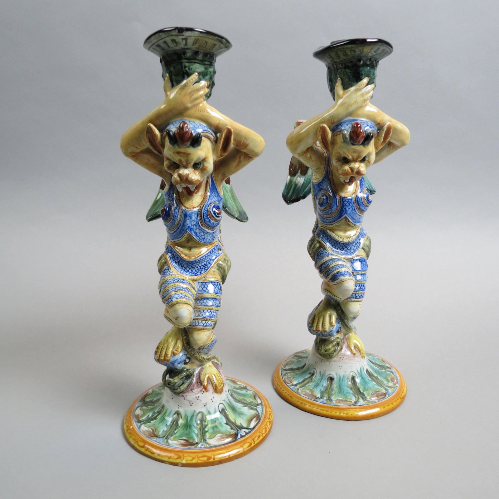 Cantagalli Italian Pottery Figural Candlesticks,: pair, Renaissance style decoration with winged creature holding an upside down helmet, rooster mark......In 1878, Ulisse Cantagalli took over the family's factory in Florence and began to trade as Man