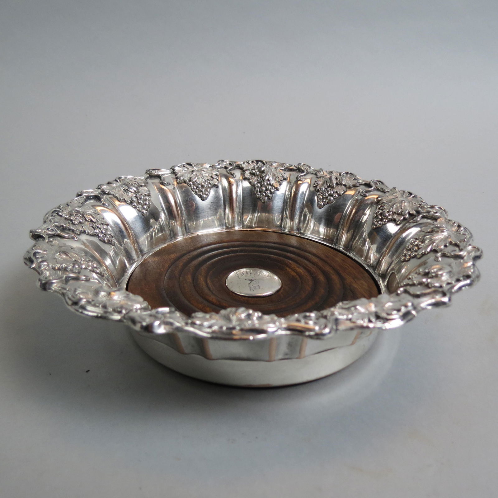English Silverplate Wine Coaster,: grape and vine design, wood liner with silver medallion having a crest, 7 3/4", 19th century.