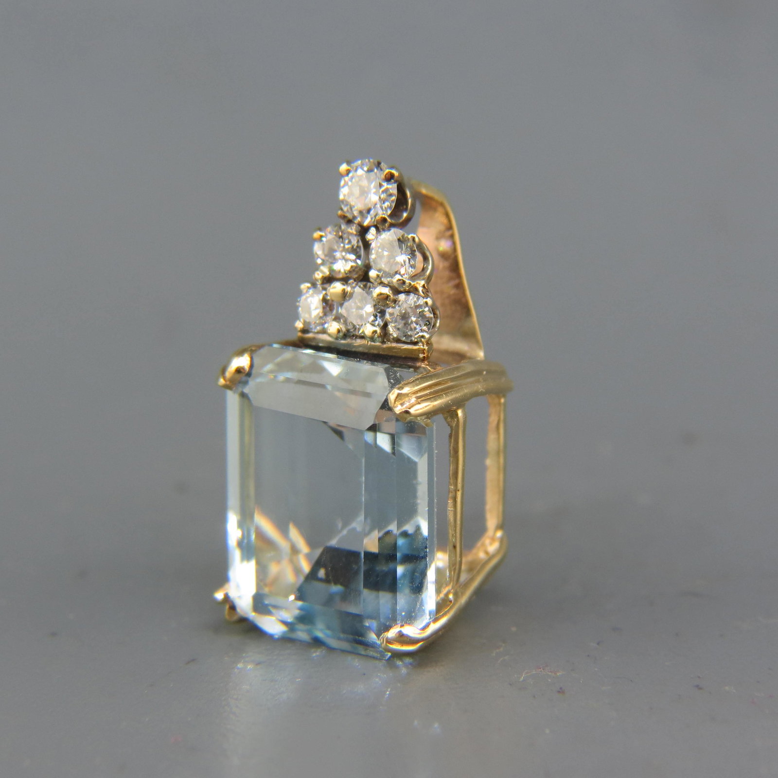 Blue Topaz & Diamond Pendant,: emerald cut gem weighing 12.25 carats with 5 round diamonds above totaling .40 carat, 14K yellow gold, with appraisal of $1,650.00, 1" long.
