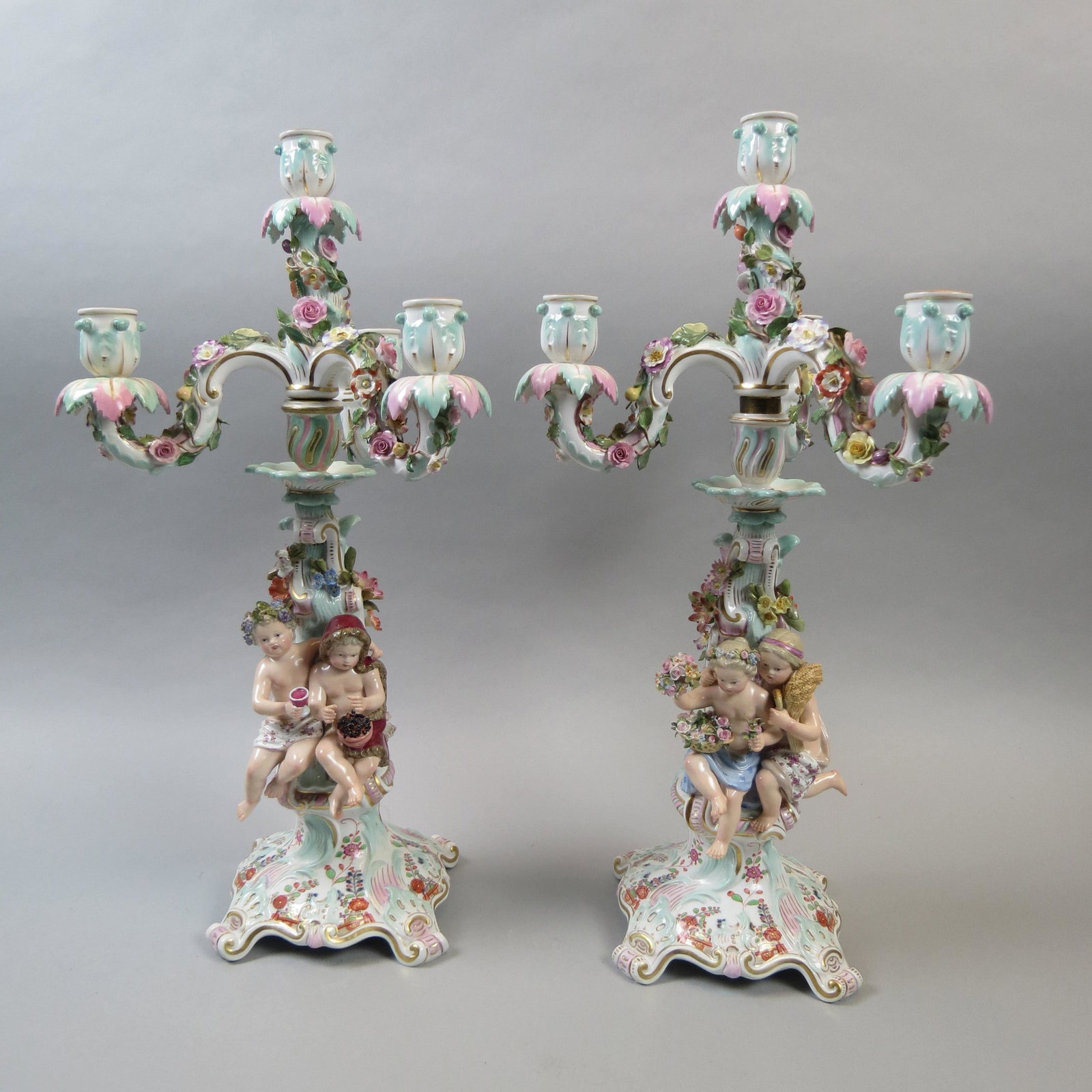Pair of Meissen Four Seasons Porcelain Candelabra: With figures of children on bases representing the four seasons, one roasting chestnuts on fire, one with wine goblet and grapevine wreath, one with sheath of wheat and other with basket of flowers, h
