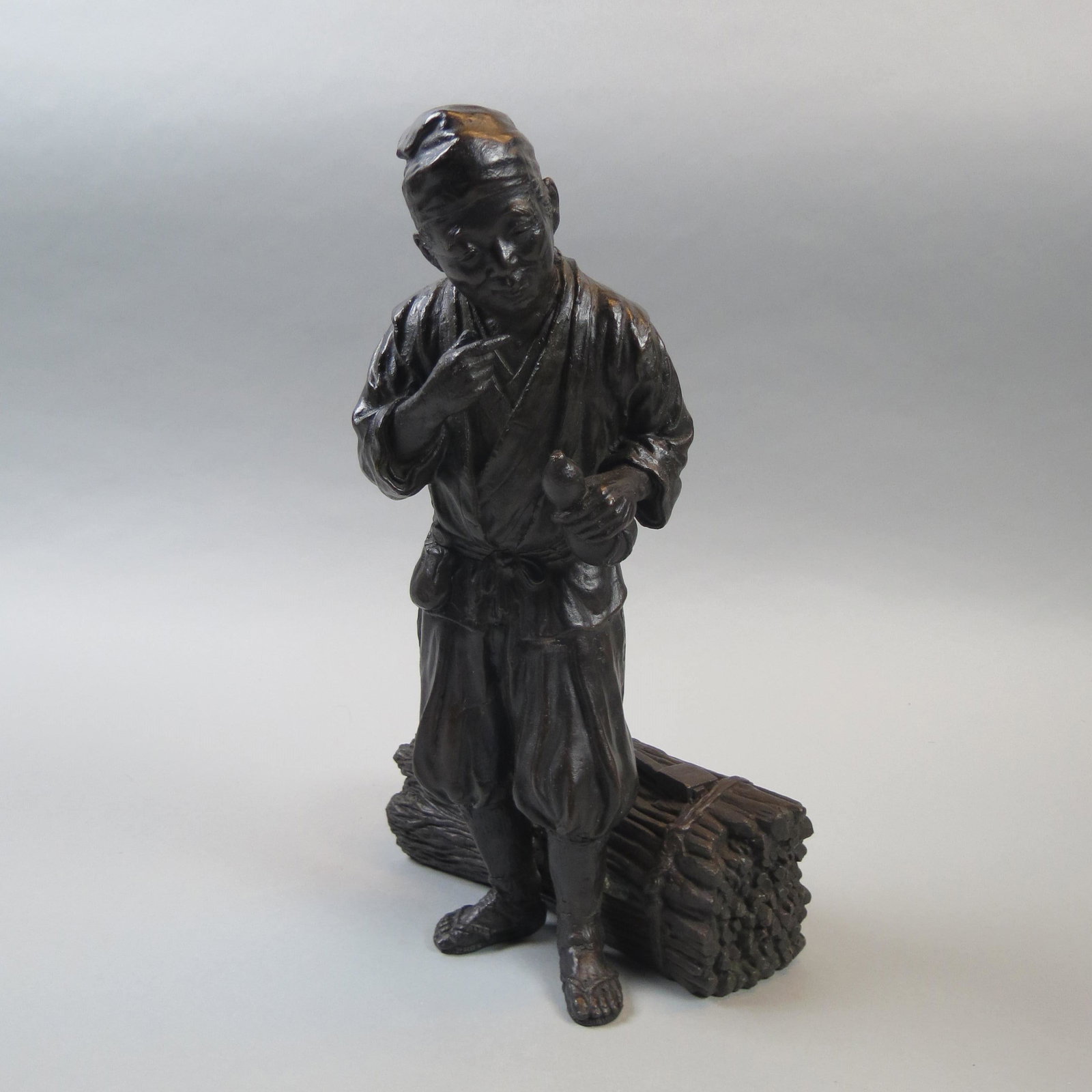 Japanese Bronze of Man with Harvest: Axe laying open bundle, standing figure holding a drinking vessel, Meiji period, circa 1880, fine detail, excellent.