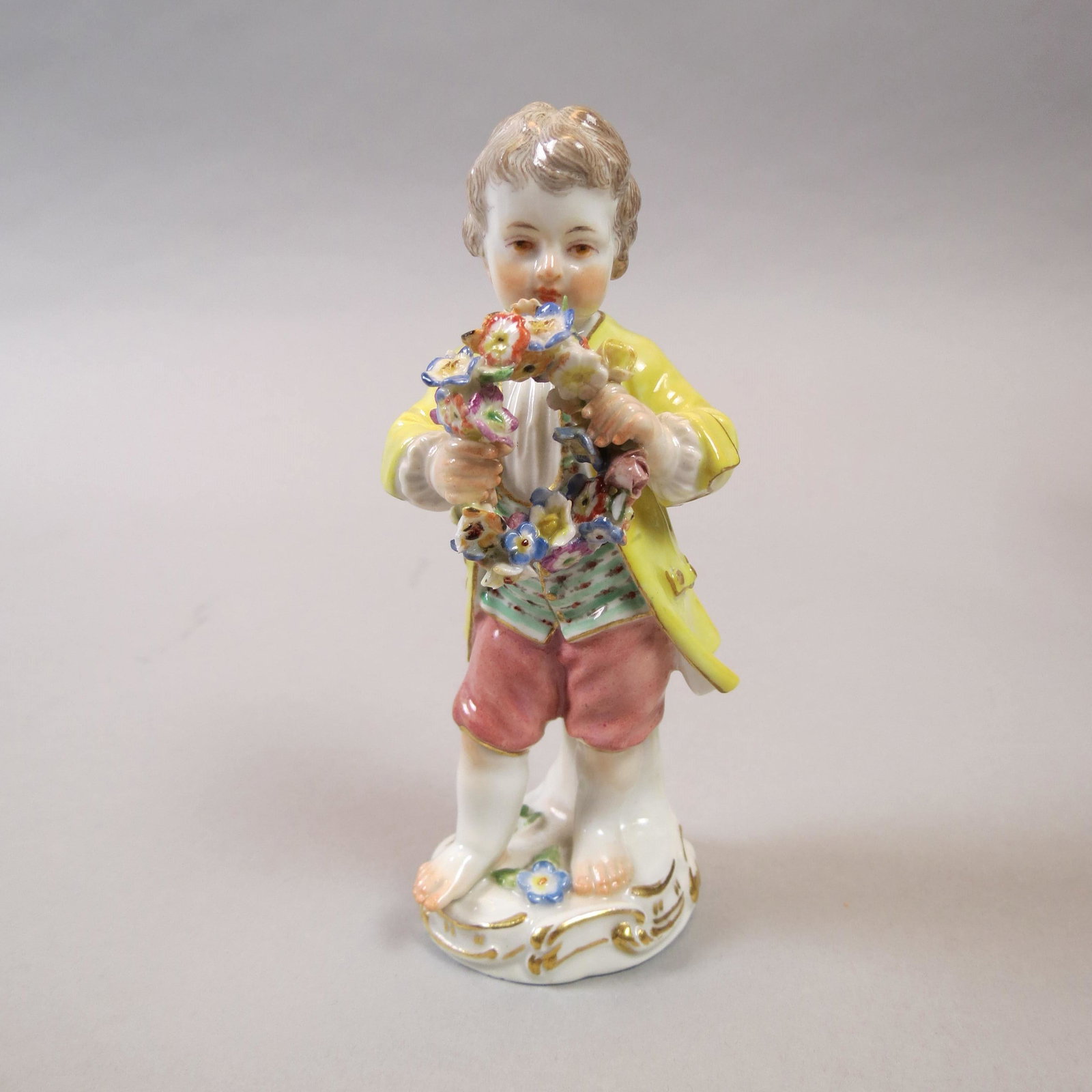 Meissen Porcelain Figurine of Boy with Wreath: Yellow coat, 5, crossed swords mark, minor petal loss.