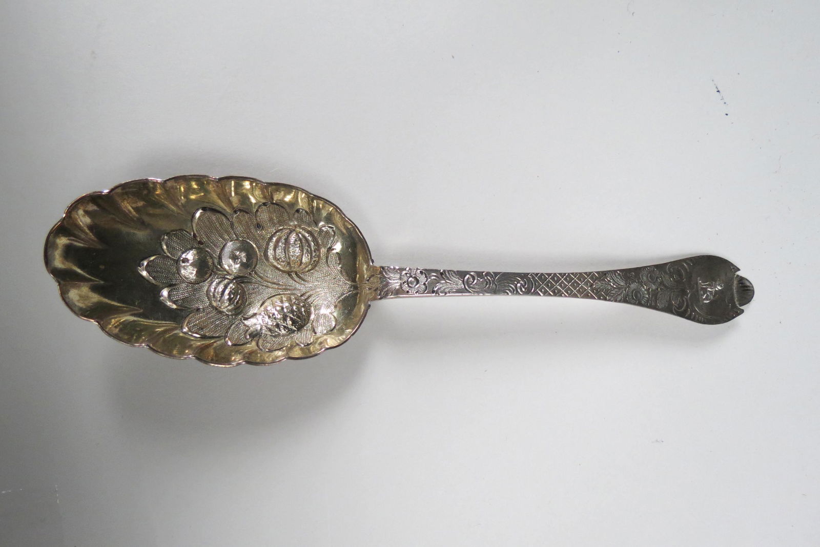 1705 English Sterling Berry Spoon,: hallmarks of Exeter, beaded rat tail pattern with raised fruit and floral in gold wash bowl, 8 1/2", crest of a seated leopard on handle, excellent.