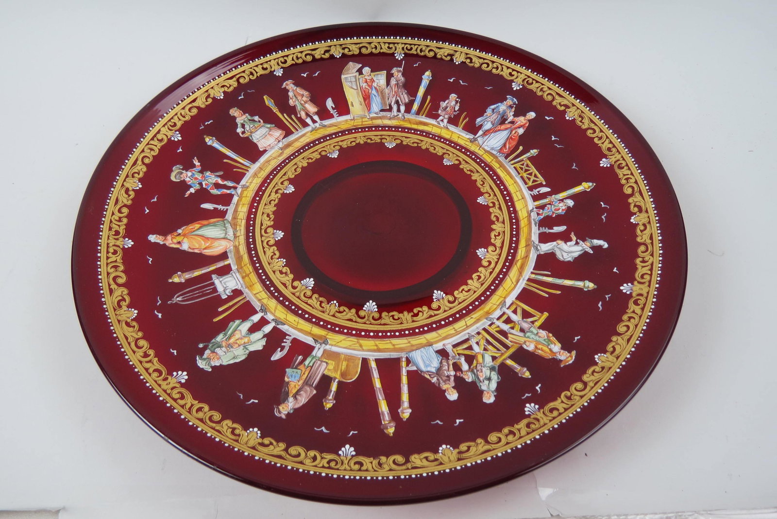 Italian Art Glass 18" Charger with Harlequin,: and Jester among Colonial dressed partygoers, fine enamel work on rich ruby, excellent.