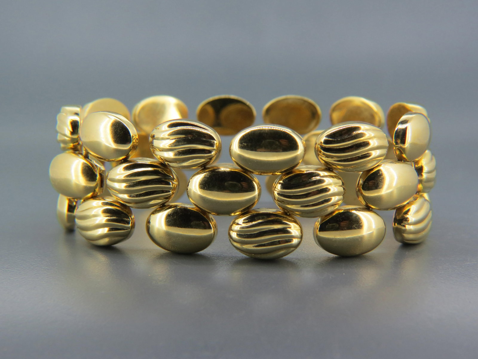 18K Gold Bracelet,: oval cabochon links with alternating plain and wavy designs in Retro style, yellow gold, 42.3 grams, signed REV, 7" long.