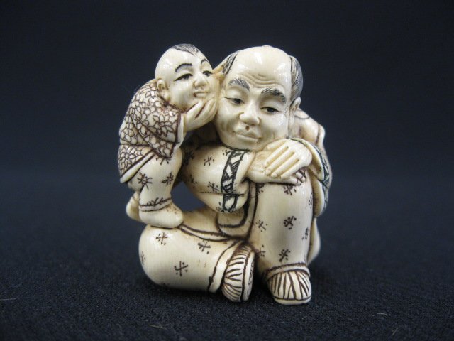 Carved Ivory Netsuke of a Young Boy,: whispering to his seated father, signed, 1 1/2".