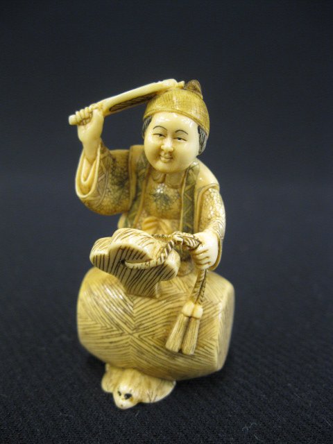 Carved Ivory Netsuke of a Man,: holding a fan while standing on a huge mallet which is resting on a lucky bat, 2 1/8", signed.