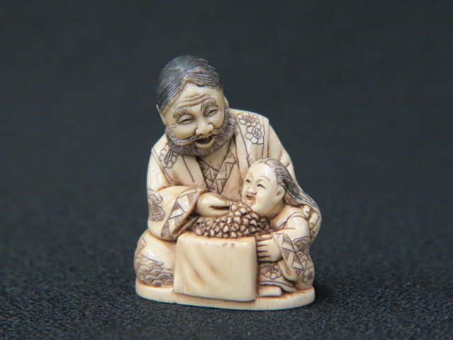 Carved Ivory Netsuke of a Seated Man,: feeding his child grapes, 1 3/4" tall, signed, excellent.