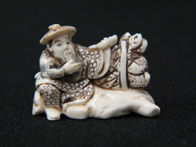 Carved Ivory Netsuke of a Fisherman,: smoking a pipe, basket full of fish by his side, 1 3/4", signed, excellent.