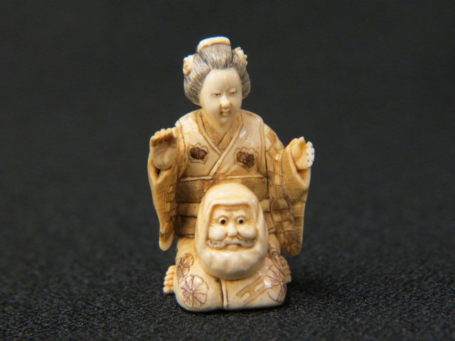 Carved Ivory Netsuke of a Kneeling Geisha,: with a Daruma doll mask on her lap, 1 3/4" tall, signed, excellent.
