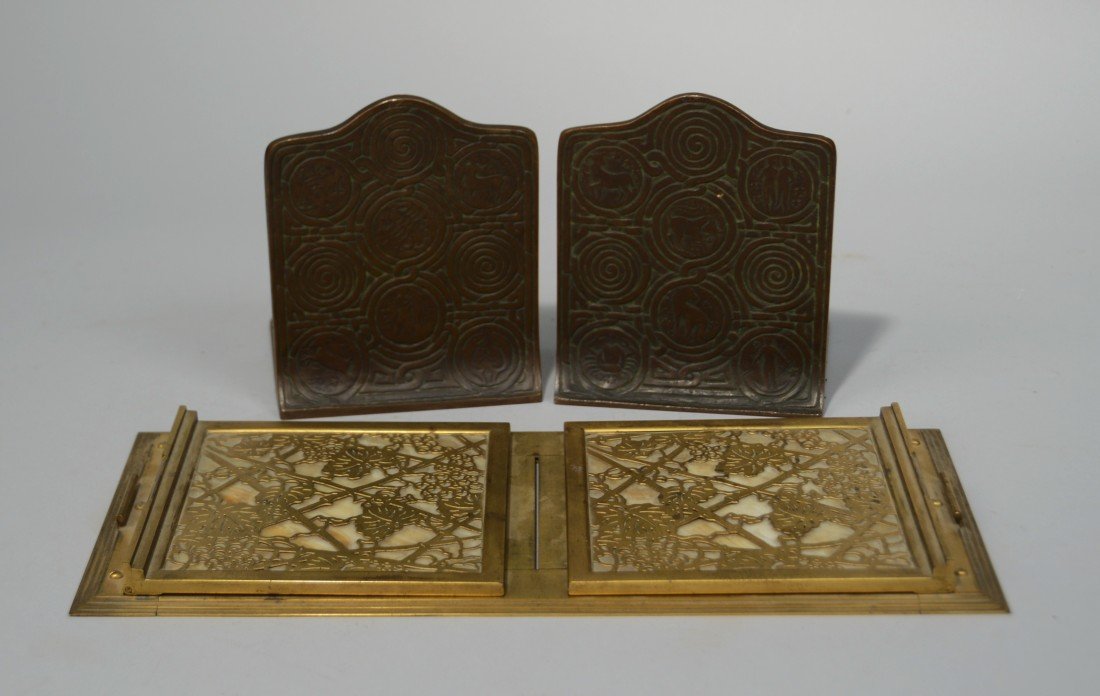 TIFFANY STUDIOS GILT BRONZE AND GLASS BOOK RACK;: TIFFANY STUDIOS GILT BRONZE AND GLASS BOOK RACK; inscribed Tiffany Studios, New York, 1027, length: 14 1/2 inches; together with a PAIR OF TIFFANY STUDIOS PATINATED BRONZE BOOKENDS, inscribed Tiffany 