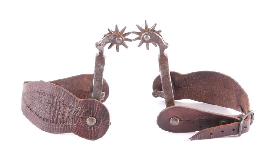 Buermann Spurs w/ Prineville Oregon Straps: This is a pair of August Buermann spurs with Prineville, Oregon tooled leather straps. The spurs are forged iron showing a drop shank and a ten point rowel. The leather straps have a hand tooled baske
