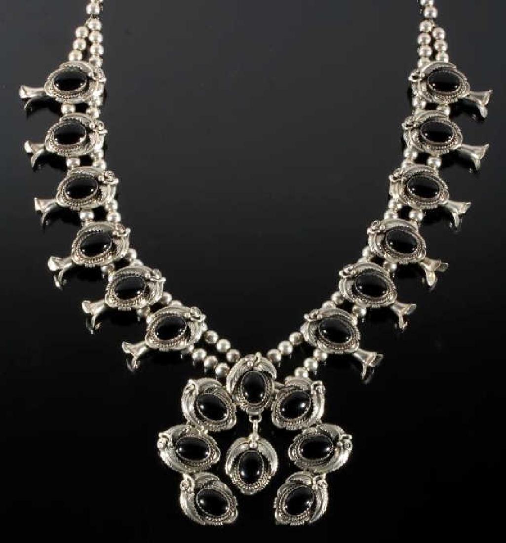 Robert Kelly Navajo Black Onyx Squash Blossom: Featured in this lot is a Navajo Native American Indian squash blossom necklace, crafted by the renowned Robert Kelly. The necklace boasts a large Naja, showing floral leaf motif, and boasting seven l