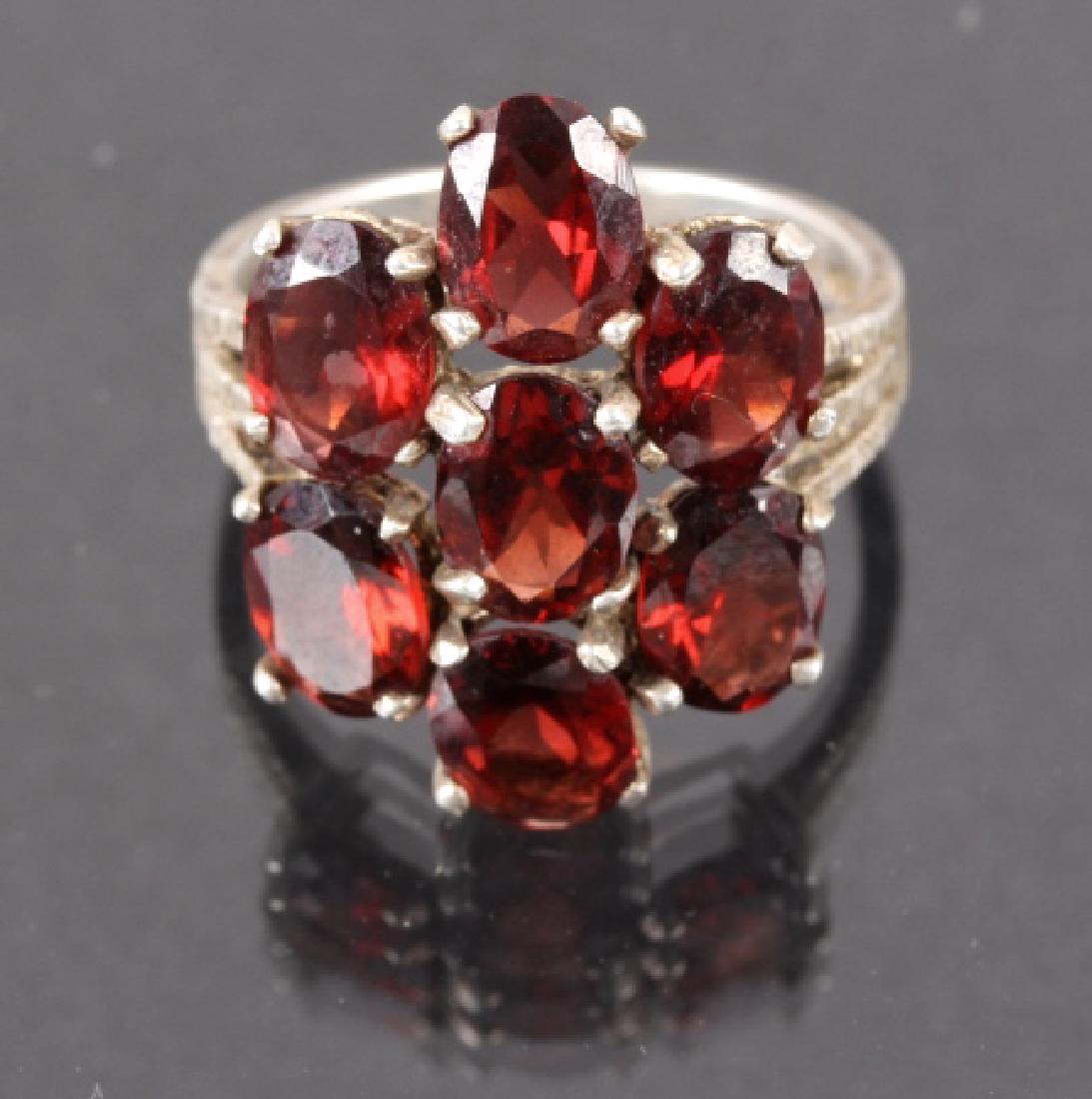 Sterling Silver Red Garnet Cocktail Ring: For sale in this lot we have a sterling silver cocktail ring with 7 embedded red garnets. This ring is adorned with a cluster of 7 red garnets on a silver band that splits in to three grooved bands ne