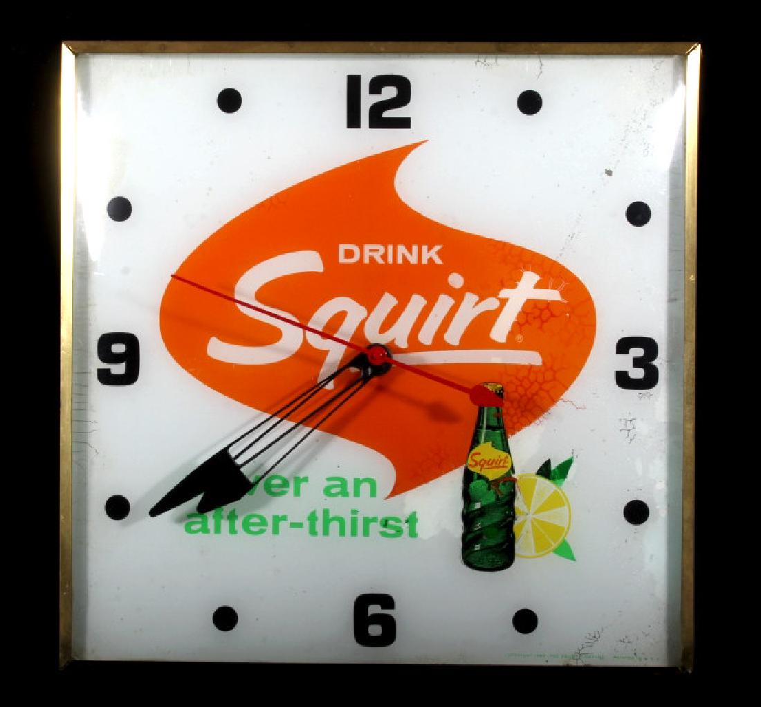 Vintage Analog Squirt Soda Advertising Clock: For bidding in this lot is a 1960's era Squirt soda illuminated analog clock, by PAM. The clock sits in a brass toned square case, and has a curved glass cover. The clock face itself shows the Squirt