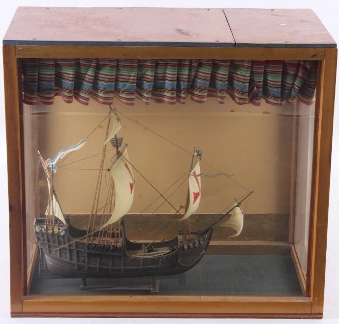 Galleon Ship Model In Display Case: In this lot we have a galleon ship model in a display case. On the ship itself there are several different coat of arms. The hull of the ship is all brown with the coat of arms attached to the bow and