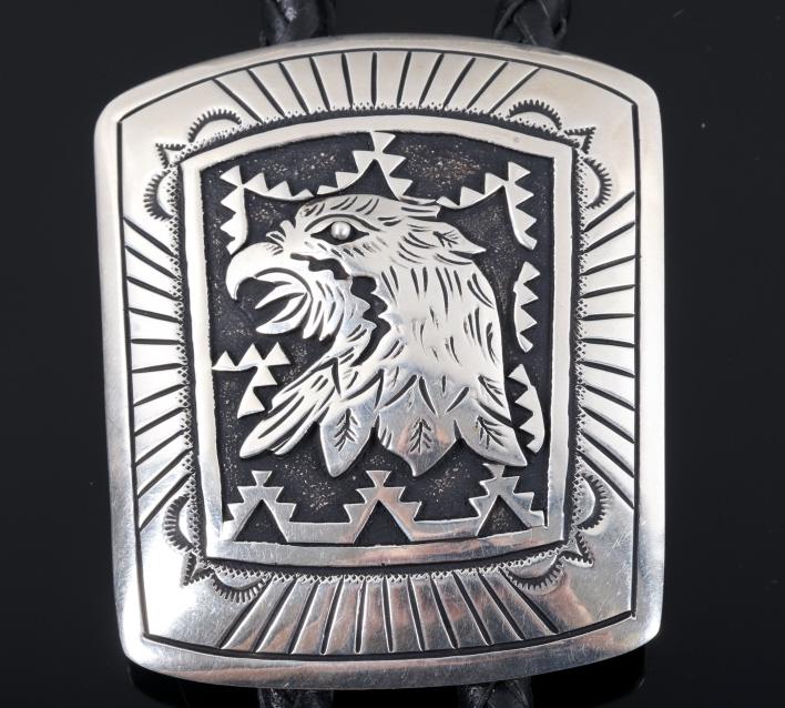 Navajo Signed T & R Singer Sterling Eagle Bolo Tie: Offered in this lot we have a Navajo Native American sterling silver eagle bolo tie signed by T & R Singer. The bolo tie is constructed out of woven black leather with sterling silver and gold cap at