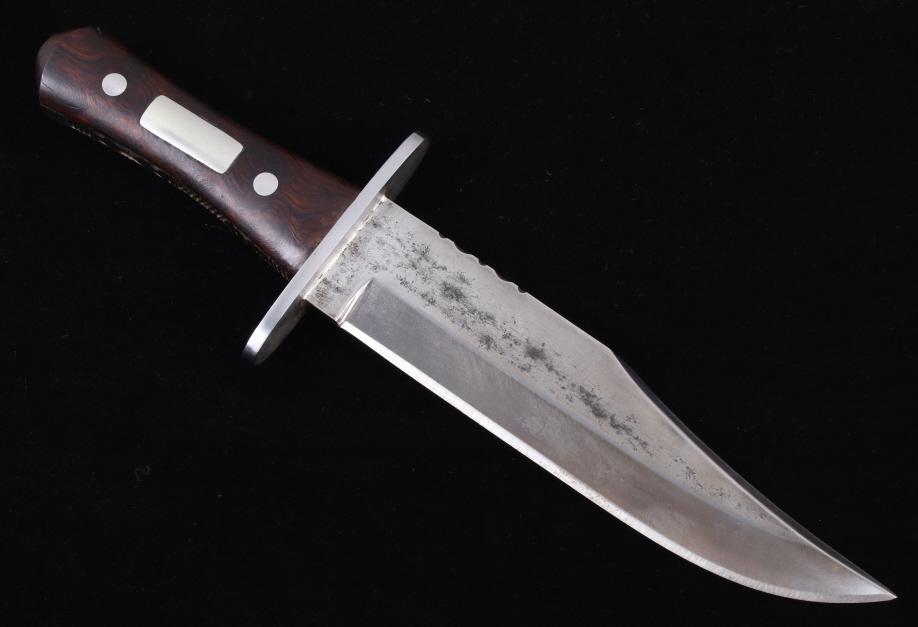 Wayne Skaggs Handmade Custom Bowie Knife W/ Sheath: Featured in this lot we have a custom handmade bowie knife by Wayne Skaggs with leather sheath. The knife shows a heavy high carbon steel clip point blade with a iron guard and wooden grip. The blade 