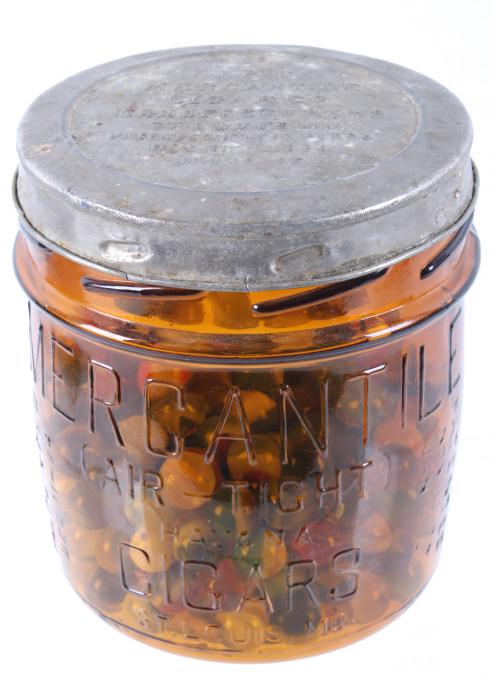 Mercantile Cigar Co. Glass Jar & Antique Marbles: Included in this lot we have a original Mercantile Cigar Co glass jar and tin lid with a collection of antique glass marbles. The jar displays glass construction with embossed lettering across the ext