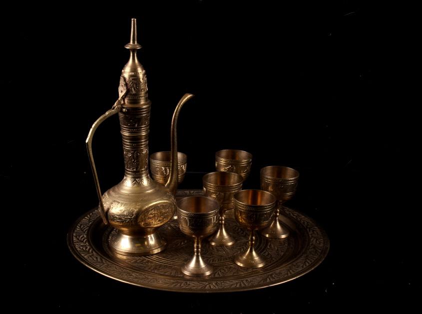 Antique Brass Ceremonial Turkish Tea Set: In this lot is an antique brass ceremonial Turkish tea set, which includes a tray, a tea pot, and six footed small cups. The tray for this set is 12" across and highly etched with a flower in the cent