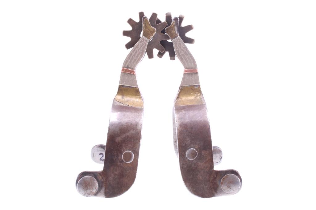 Chandler Silver & Brass Gal Leg Spur Pair: Featured in this lot is this Chandler silver and brass ladies leg spur pair. The pair shows a mixture of metals decorating the spur, with spur strap lugs and heel strap lugs present on both sides of t