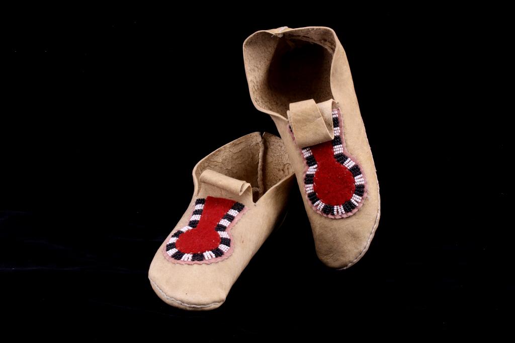 Montana Crow Key Hole Beaded Moccasins c 1940-1950: This lot features a set of hide beaded moccasins from the Montana Crow Native American Indians and dating to circa 1940-1950’s. The piece shows an Indian tanned hide with very unique one piece const
