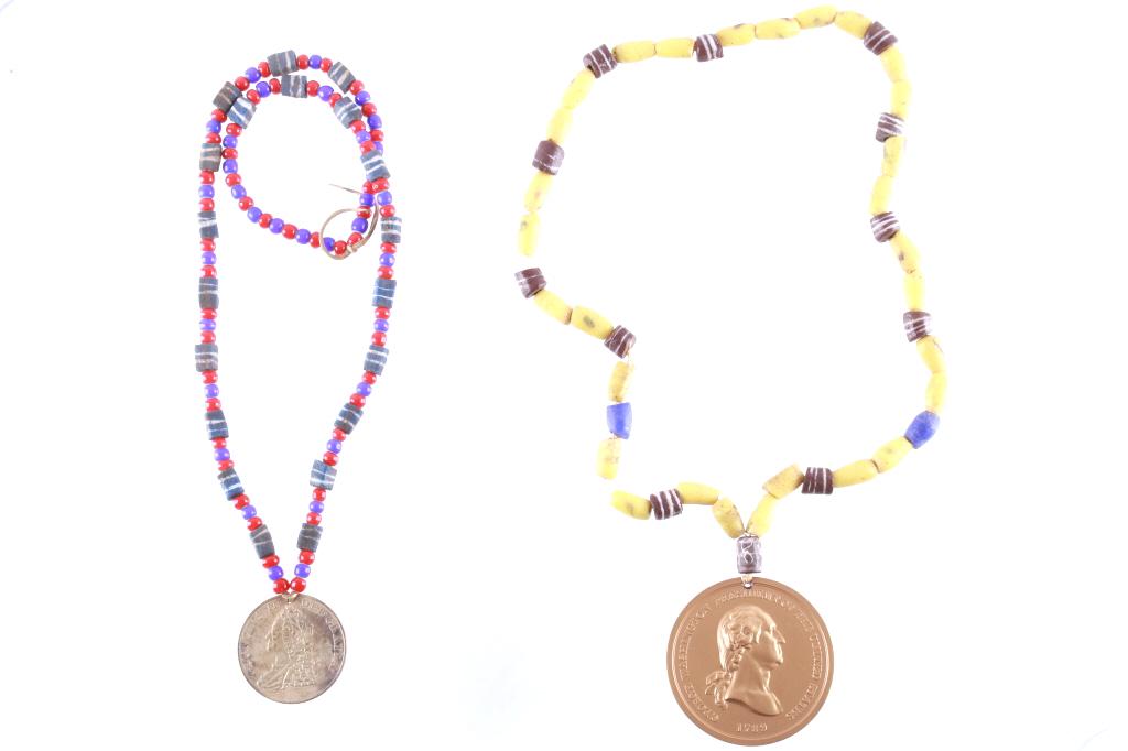 King George George Washington Indian Peace Medals: Offered in this lot are two Indian Peace Medals on trade bead necklaces. The first is a King George II medal stamped 1757. This medal is struck in a brass tone and measures 50mm. The face side shows K