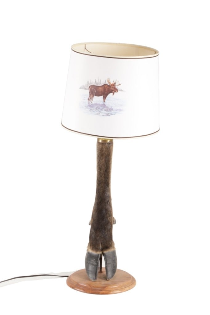 Montana Moose Leg Taxidermy Lamp c. 1960's: Featured in this lot is this Montana moose leg taxidermy lamp circa 1960's. the lamp features a wonderfully crafted moose leg taxidermy, wooden shield and brass fixture construction that shows a thru-