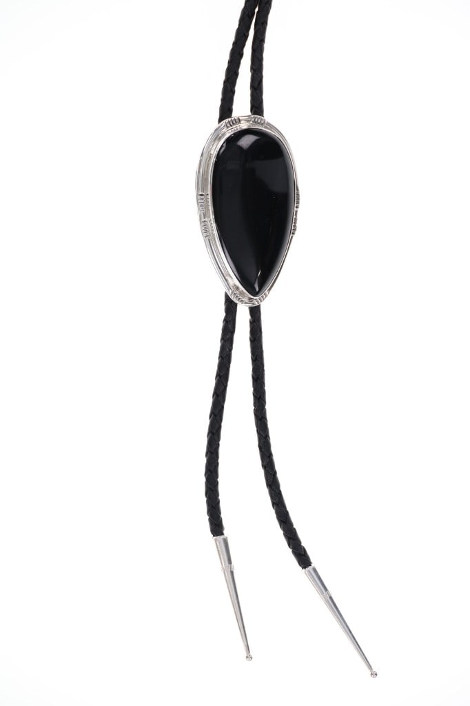 Navajo C.C. Tsosie Sterling Silver Onyx Bolo Tie: Featured in this lot is this sterling silver onyx bolo tie from Navajo artist Clayton Chez Tsosie. The bolo tie features a wonderfully and professionally crafted sterling silver, onyx, and braided lea