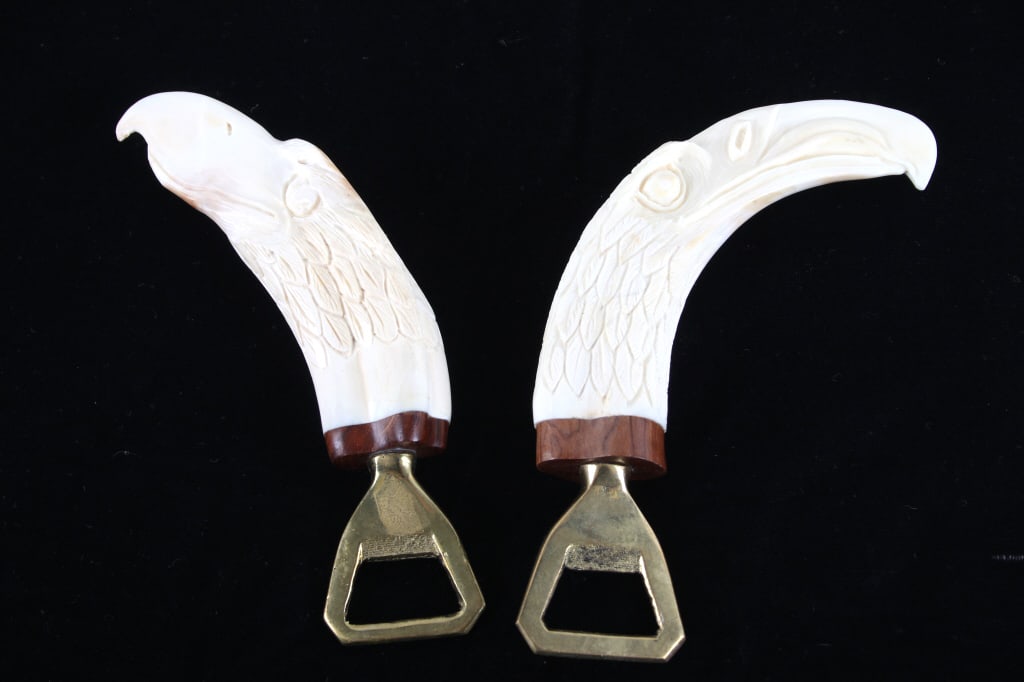 Carved Eagle Boar Tusk Bottle Openers (2): Presented in this lot are Hand Carved Eagle Boar Tusk Bottle Openers (2). Popular for their unique, rustic aesthetic and durable construction, these boar tusk bottle openers feature a wonderfully and 