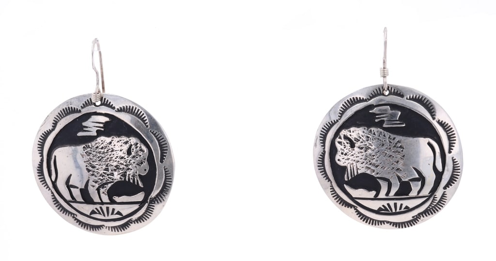 Navajo T&R Singer Sterling Silver Buffalo Earrings: Featured in this lot is this pair of sterling silver buffalo mural earrings from Navajo artists Tommy and Rose Singer. The earrings feature a wonderfully and professionally crafted sterling silver con
