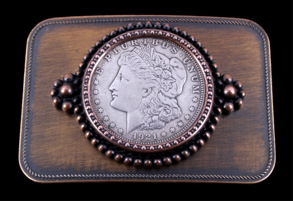 Morgan Silver Dollar 1921 Belt Buckle: The lot features an original 1921 Morgan Silver Dollar set on a copper washed western belt buckle. The cowboy belt buckle shows good condition. The coins mint is unknown. Buckle is 2.25"x3.25"